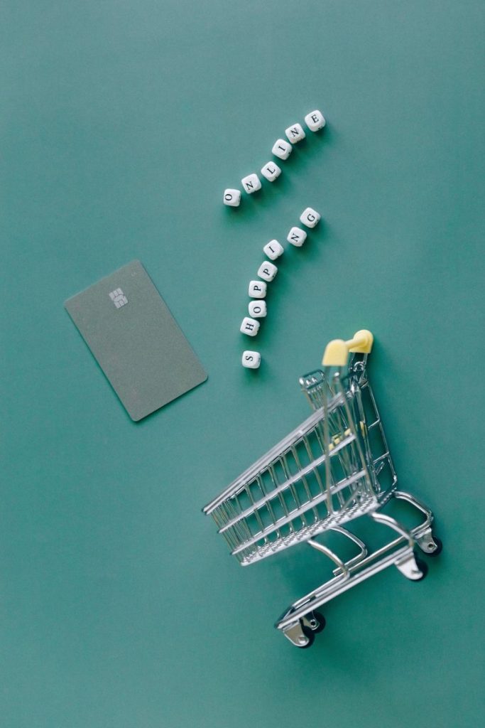 A conceptual image featuring a mini shopping cart, credit card, and letter blocks spelling 'online shopping' on a green background.
